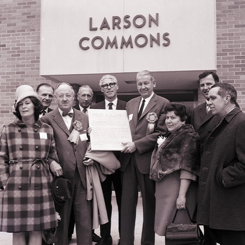 A black and white photo of a group of people standing outside of the old Larson Commons with a plaque.