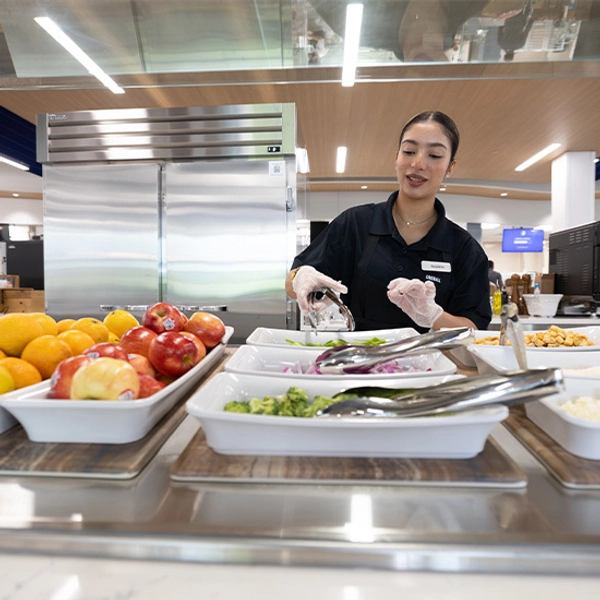 A worker at Larson Commons using tongs to grab vegetables.