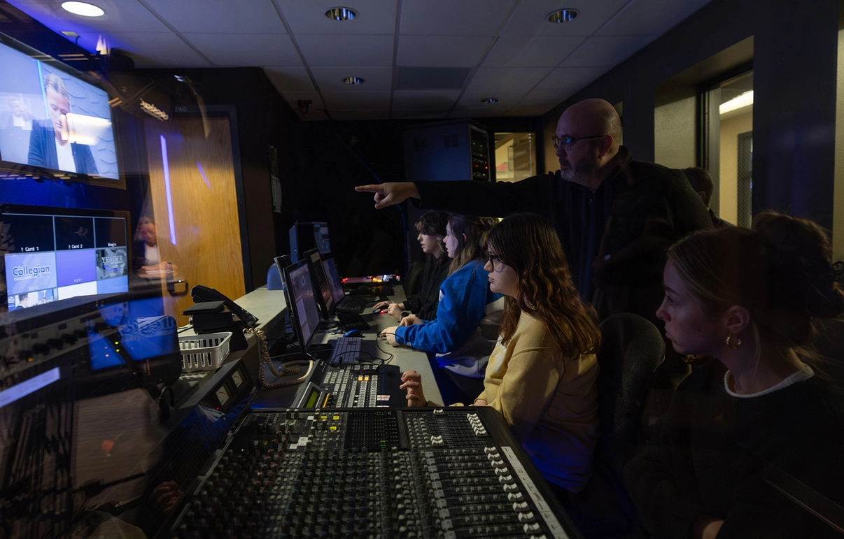 Students editing videos in the studio in Yeager Hall while a professor helps and instructs them.