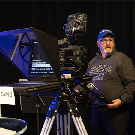 A professor operating a large camera with teleprompter.