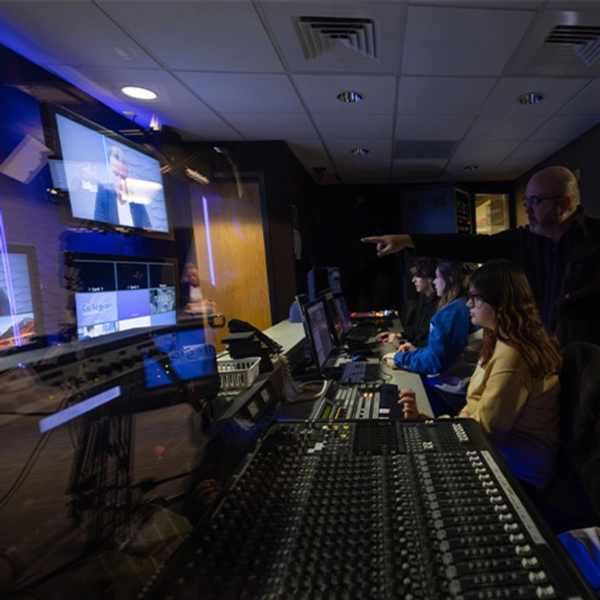 Students editing videos in the studio in Yeager Hall while a professor helps and instructs them.