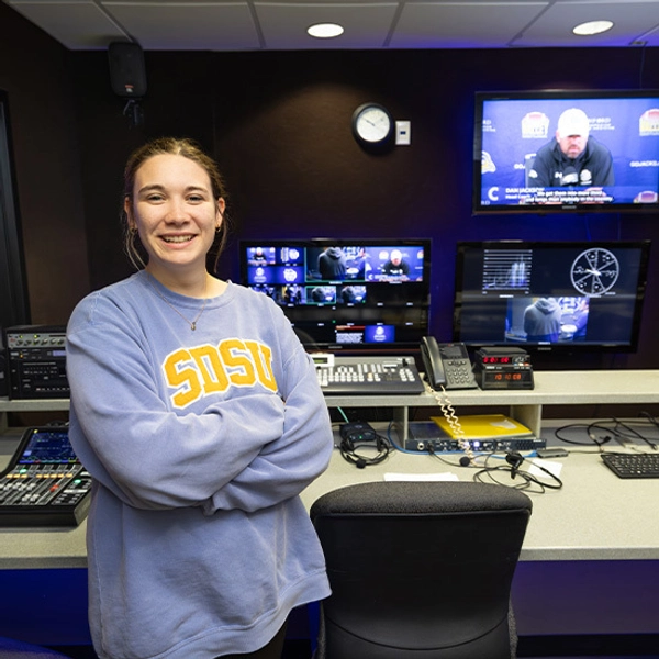 A female student smiles and poses in front of editing equipment.