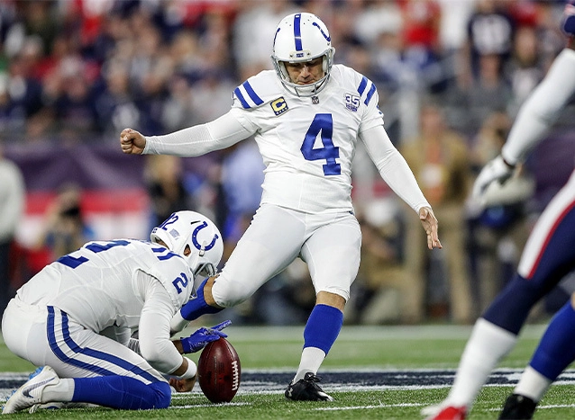 Former Indianapolis Colts kicker Adam Vinatieri strikes the ball as a teammate holds it on the turf.