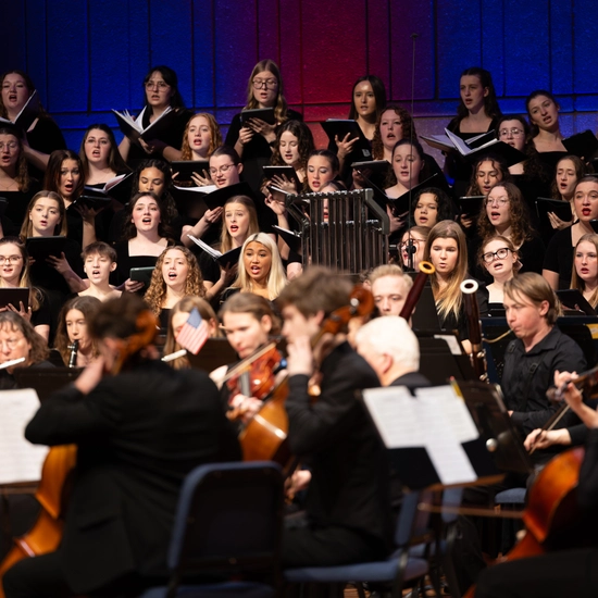 A choir and an orchestra perform on stage together.