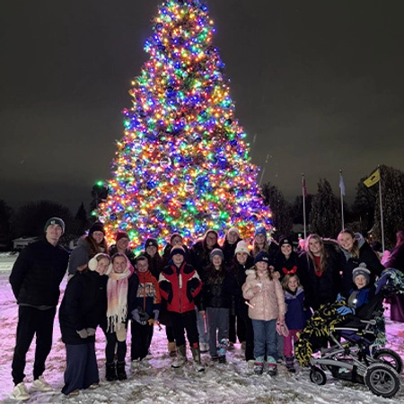 State a thon members stand together in front of a beautifully lit, outdoor Christmas tree