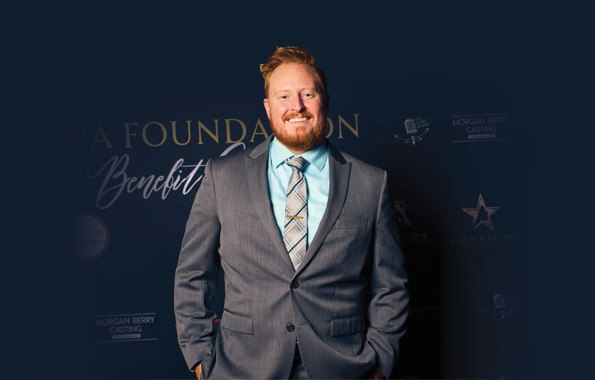 Thomas Hagena smiles in a suit and tie at an event in front of a step and repeat banner.