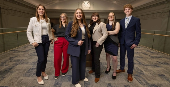A group of six SDSU students stands together in Lincoln Hall, wearing professional clothing.
