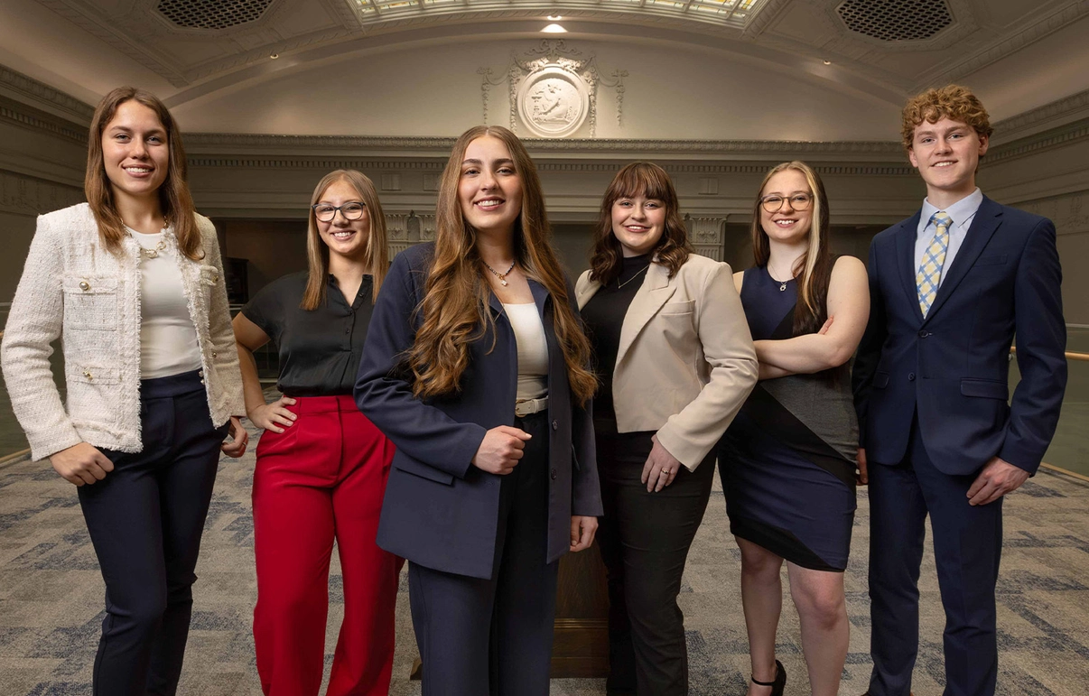 A group of six SDSU students stands together in Lincoln Hall, wearing professional clothing.