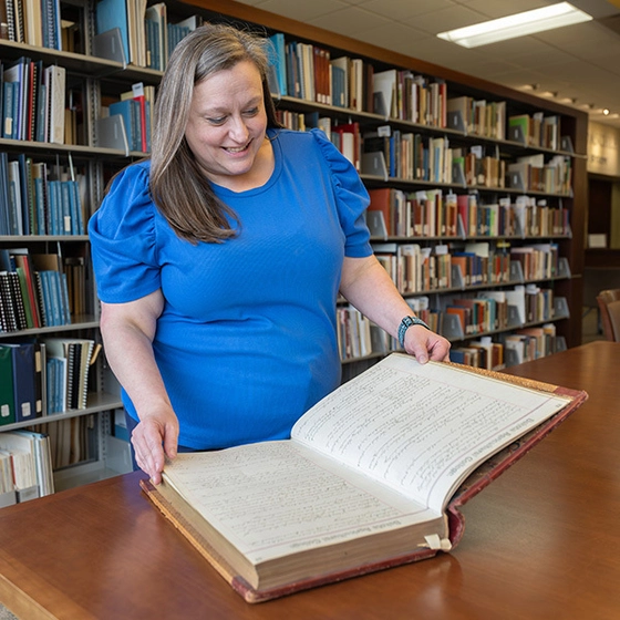A person stands at a table, flipping through a large book.