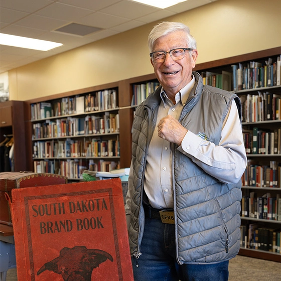 Myron Sonne stands smiling in the Briggs Library with a brand book in the foreground.