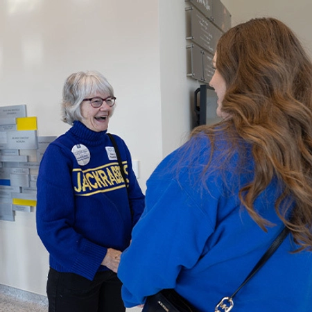 A lady smiles while talking with another during an event.