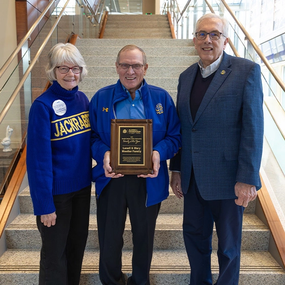 Mary and Lon Moeller stand with President Dunn and smile while holding the Family of the Year plaque.