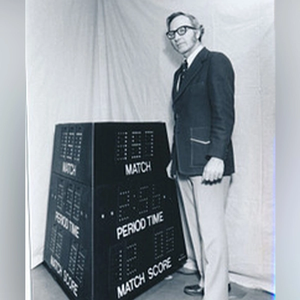 A man stands next to a wrestling scoreboard prototype, which eventually morphed into Daktronics.