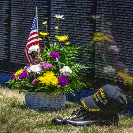 The Wall that Heals during the day, with flowers and a Vietnam baseball hat in the foreground laying on the grass.