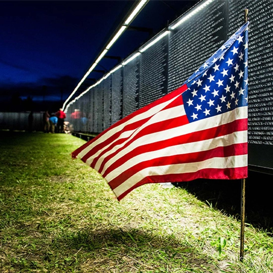 The Wall that Heals at night, lit up with an American flag in the foreground.
