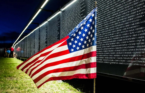 The Wall that Heals at night, lit up with an American flag in the foreground.