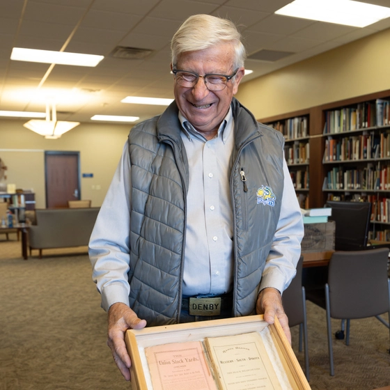 Myron Sonne smiles as he holds a display case with two documents in a library.