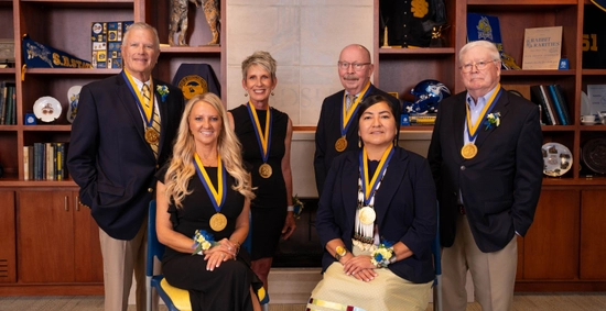 Six people wearing medals pose in front of a fireplace in Jensen-Smith Board Room at the SDSU Alumni Center.