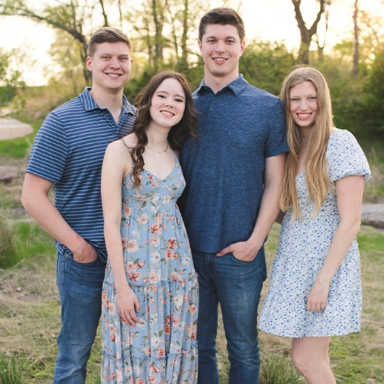 Four young adults stand outdoors on a sunny day, smiling warmly.