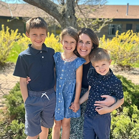 Jenn McCloud smiles with her three children in a garden space.