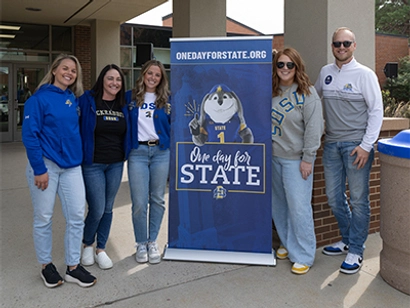 5 members of the SDSU Alumni & Foundation team smile together with a One Day for STATE sign