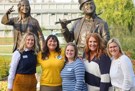 Group of five SDSU Alumni & Foundation team members stand together smiling in front of the Weary Wil and Dirty Lil statues.