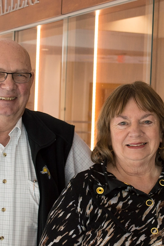 Keith and Glynn Bartels smile together in front of the Bartels Alumni Gallery.