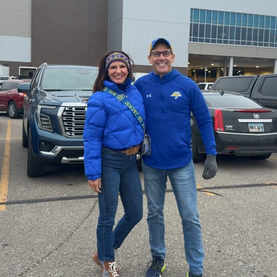 Tracy and Wes Chambers are smiling for the camera in the parking lot outside of Dana J. Dykhouse Stadium.