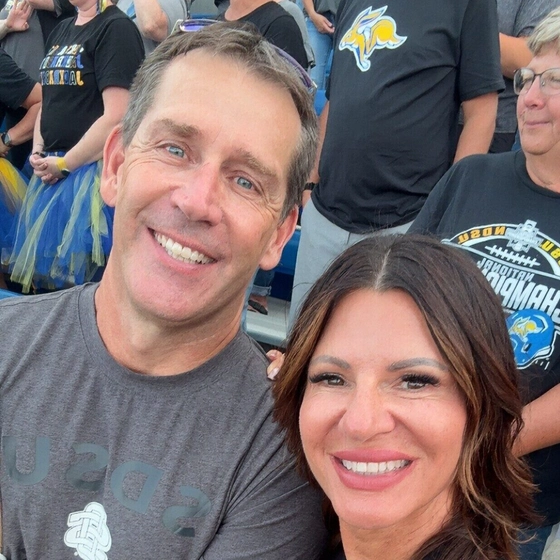 Wes and Tracy Chambers smile for a selfie at a football game in the stands of Dana J. Dykhouse stadium.