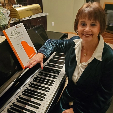 Donna Dettman sitting beside a piano, resting her hand on it.