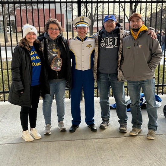 Five smiling people, including Evan Bartelt in the center, pose for a photo at the Dana J. Dykhouse Stadium.