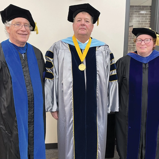 Three individuals in academic regalia stand indoors.