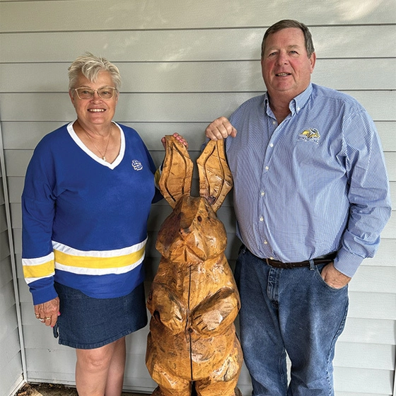 Cindy and Randy Frederick standing on their porch with a large wooden rabbit sculpture.