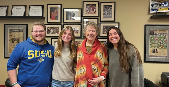 Four people stand closely together, smiling warmly at the camera.