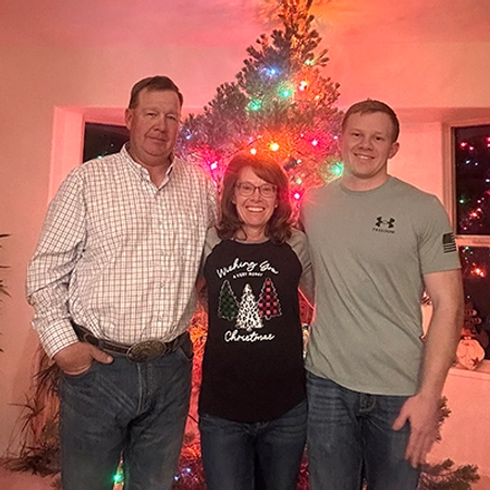 Kole Hawkins stands in front of a multi-color lit Christmas tree with his mother and father next to him.