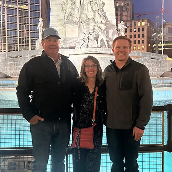 Kole Hawkins stands next to his mother and father in front of a water feature and a large marble statue.