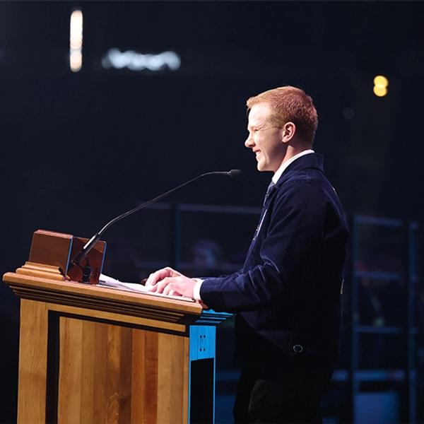 Kole Hawkins stands on stage, smiling behind a podium during his time as a Colorado State FFA Officer.