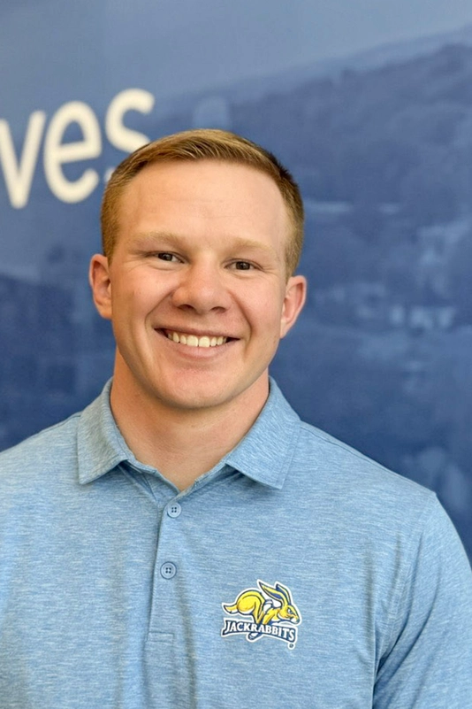Kole Hawkins dressed in a Jackrabbit shirt, smiling in front of blue wall that says "Where Loyalty Lives."