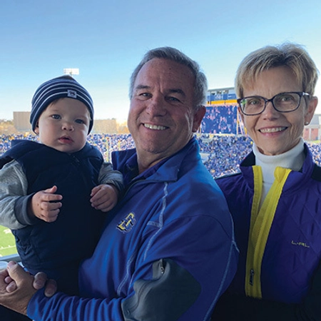 Scott and Lani Ramsdell smiling with their grandchild at a football game.