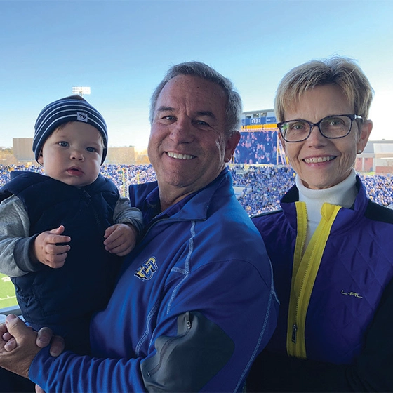 Scott and Lani Ramsdell with one of their grandchildren smiling for the camera at an SDSU football game.