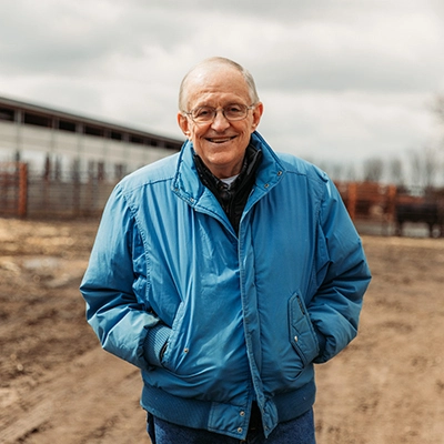 a photo of Jim Woster smiling at the camera while standing in a cattle feedlot