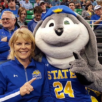 A photo of Kim Tyler and Jack the Jackrabbit mascot holding up #1 and smiling for the camera.