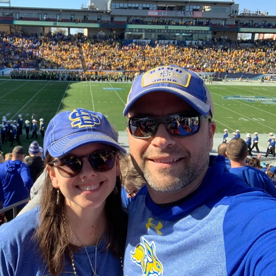 Jeff and Lori Skinner smile together at the FCS national championship in Frisco, TX with the field in the background.