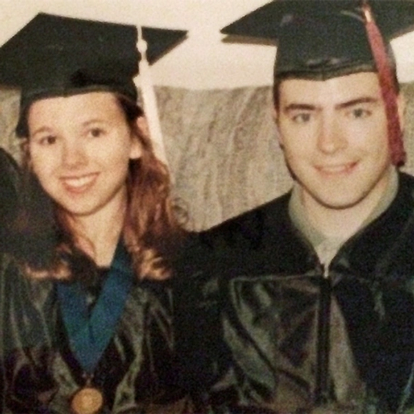 Jeff and Lori Skinner smile and sit on a couch wearing their commencement caps and gowns.