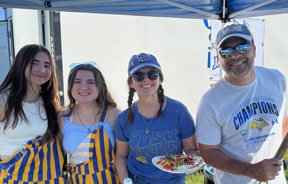 Jeff and Lori Skinner smile with their two daughters at a tailgate.
