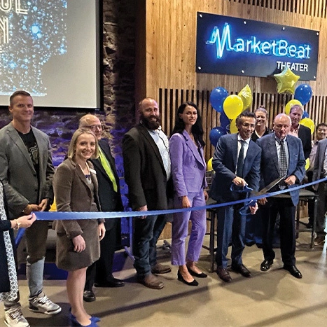 A group of people gathers for a ribbon-cutting ceremony in front of "MarketBeat Theater."