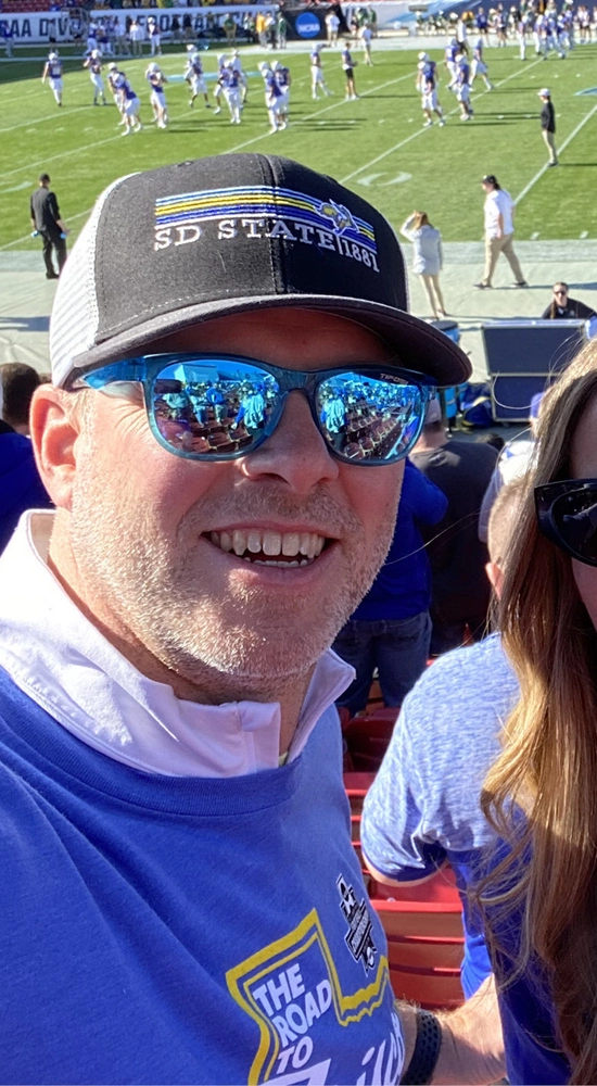 Tim Vanderham and his partner, Marci, wearing SDSU apparel and sunglasses at an SDSU football game.