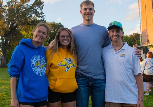 Four SDSU students smile with their arms around each other, wearing jackrabbit gear