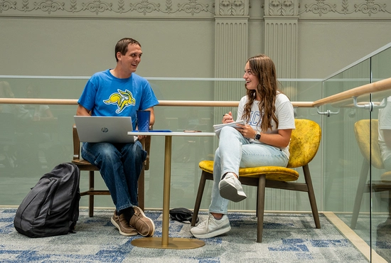 Two students in Lincoln Hall talking with one another and sitting at a small table