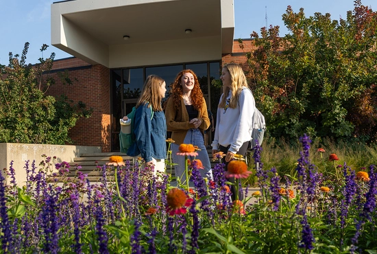 Three students standing chatting outside of Rotunda with flowers in the foreground